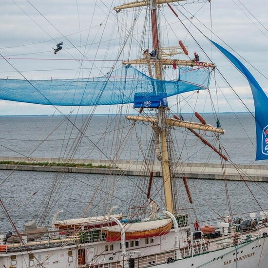 Slackliner wykonujący backflip na linie podczas pokazu Red Bull Slackship na żaglowcu Dar Młodzieży w porcie