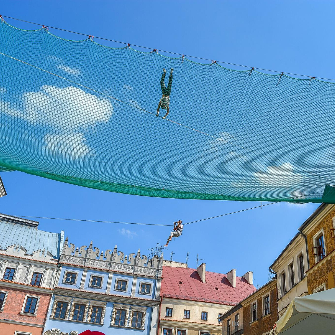 Slackliner na linie z siatką zabezpieczającą na tle kamienic Starego Miasta w Lublinie podczas Urban Highline Festival