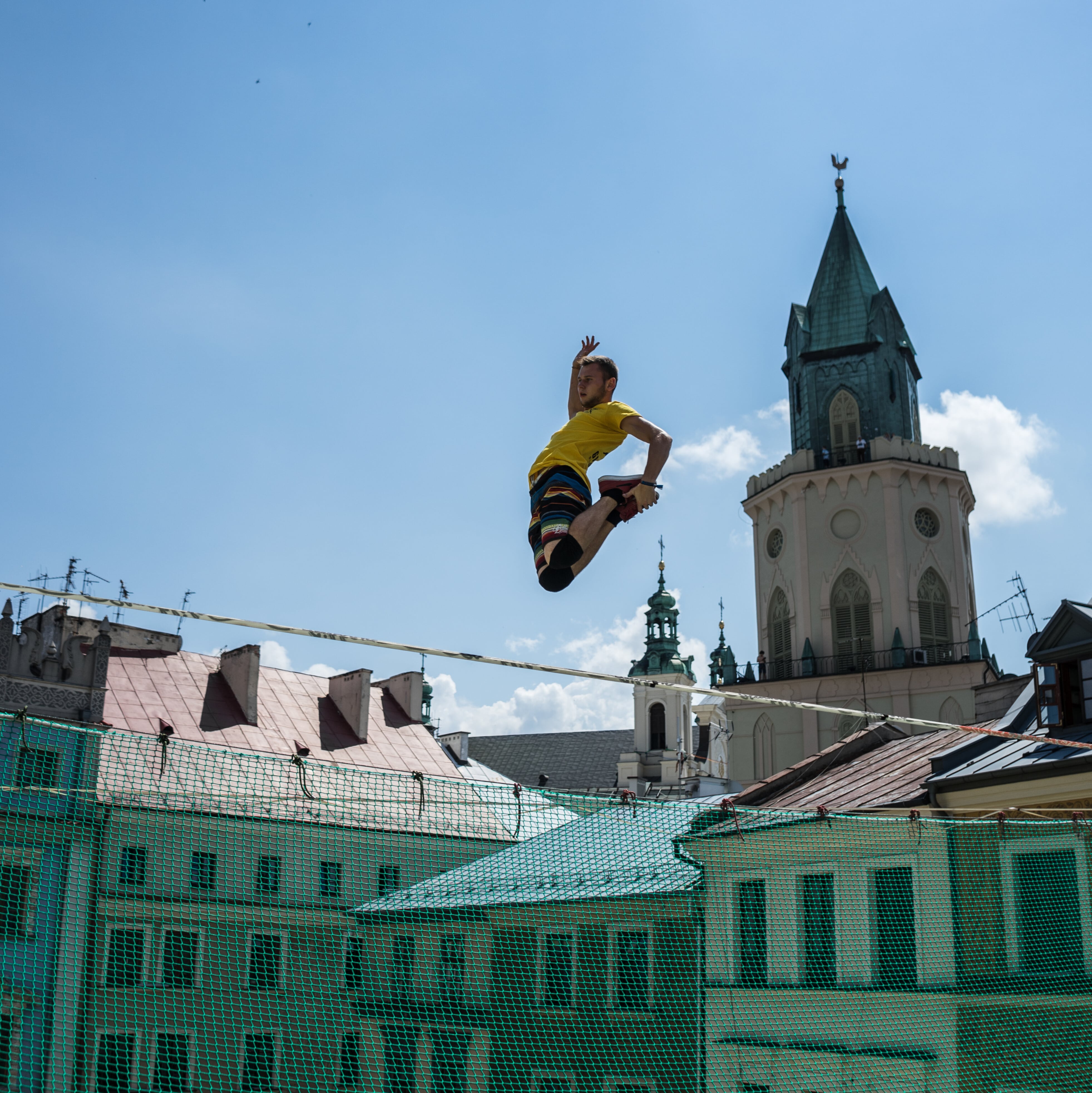 Slackliner wykonujący skok na linie w centrum Lublina na tle wieży kościoła podczas Urban Highline Festival